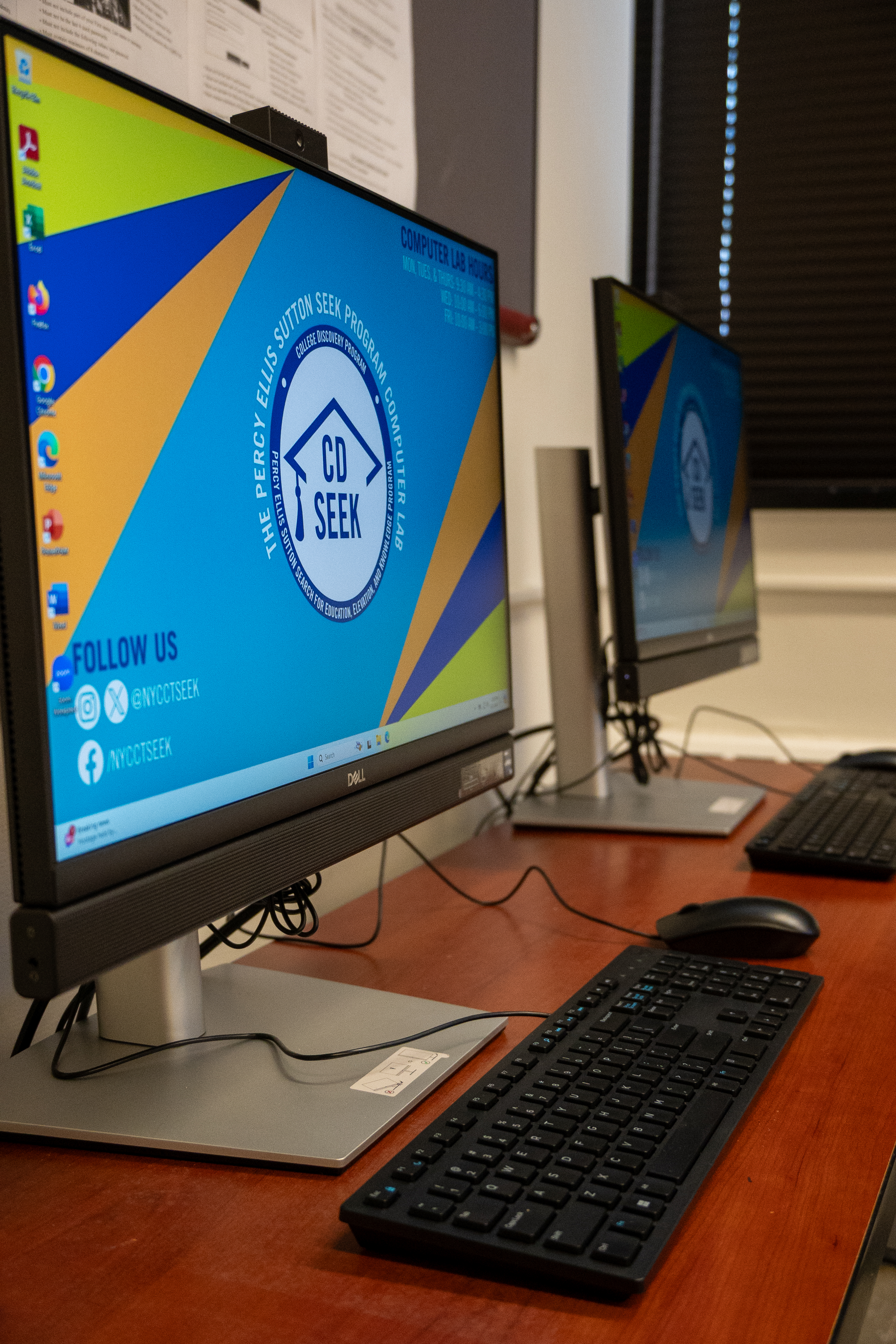 Two computer monitors, keyboards, and mice on a dark brown desk in the SEEK Computer Lab.