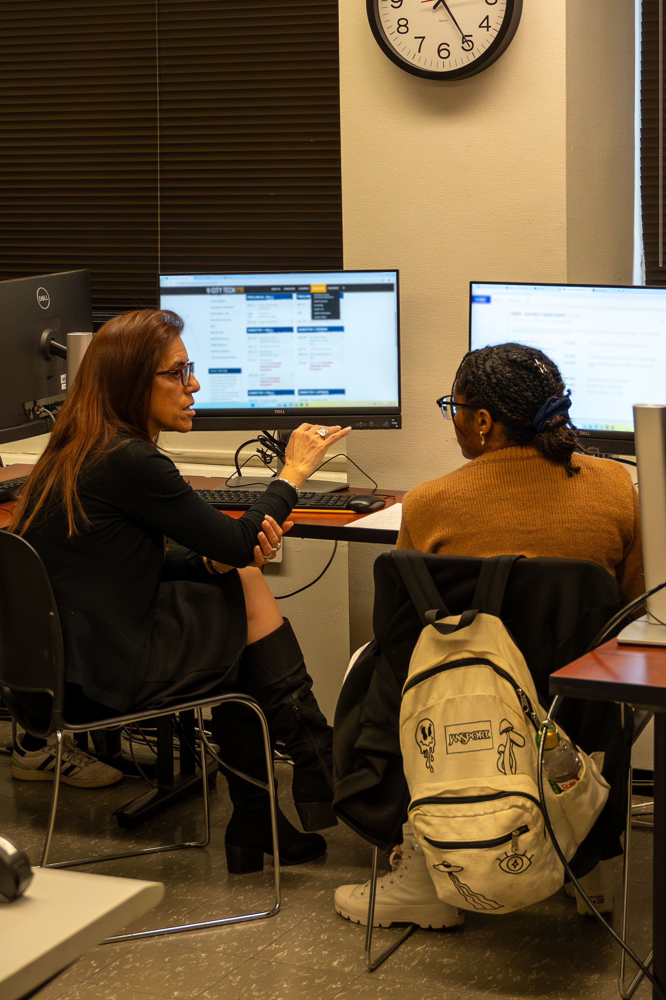 A student and a professor sitting at two computers having a conversation.